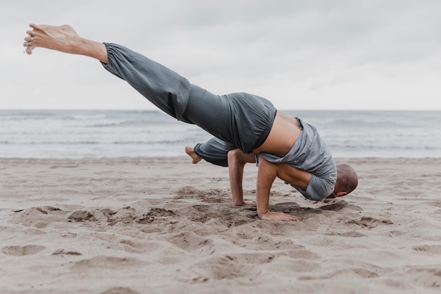 Foto hombre en la playa practicando posiciones difíciles de yoga