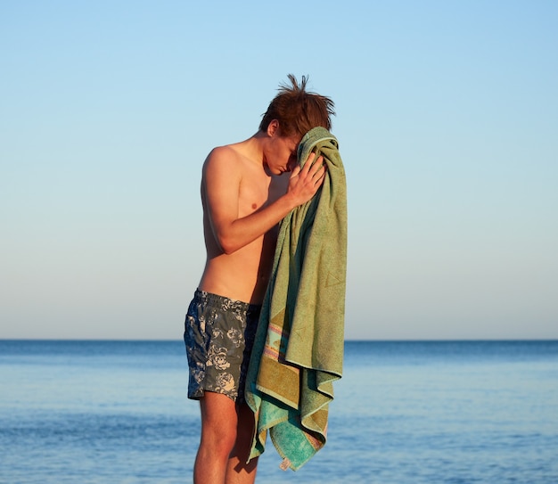 Un hombre en la playa secándose con una toalla verde