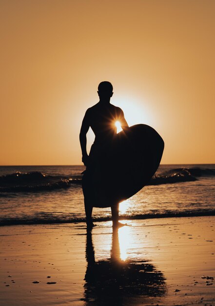 Foto un hombre se para en una playa con una tabla de surf frente a él.