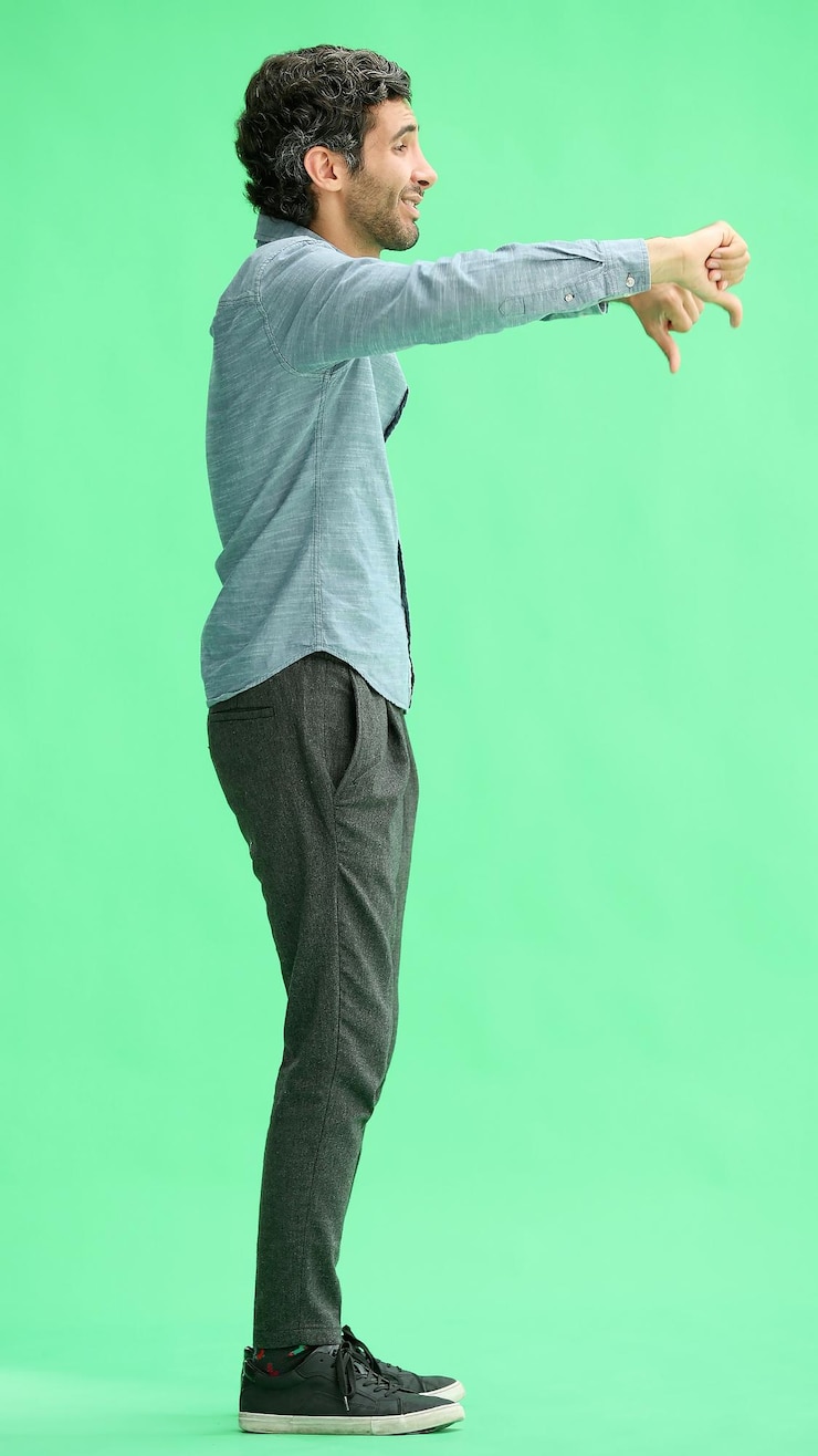 Foto hombre en pleno crecimiento aislado en fondo verde mostrando un mal signo con el pulgar