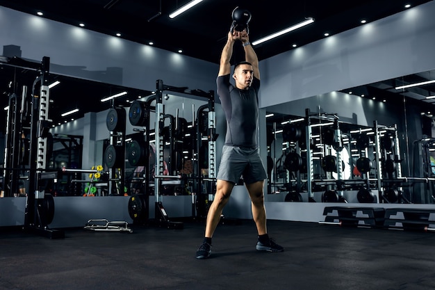 Un hombre poderoso levanta una campana de agua sobre su cabeza en el gimnasio con movimientos fuertes. El concepto de entrenamiento funcional de cross-fit. Impulso de energía