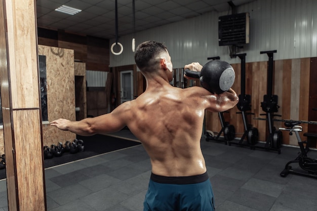 Un hombre poderoso y musculoso haciendo ejercicio con pesas rusas pesadas en un gimnasio cruzado. Entrenamiento funcional con pesas libres