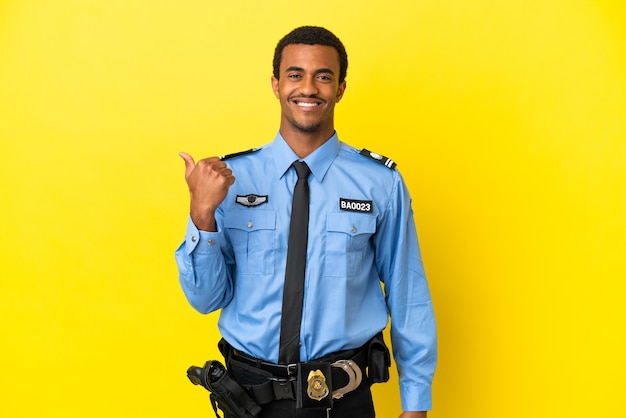 Hombre de la policía afroamericana sobre fondo amarillo aislado apuntando hacia el lado para presentar un producto