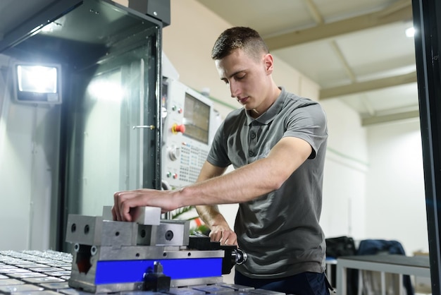 un hombre pone una pieza de aluminio en una máquina cnc y prepara una máquina de procesamiento.