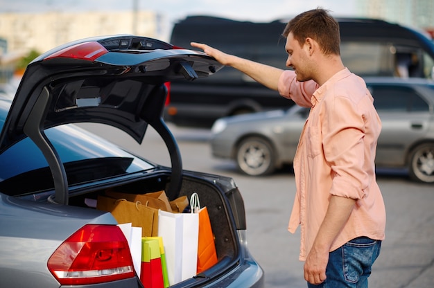 El hombre pone sus compras en el maletero del estacionamiento