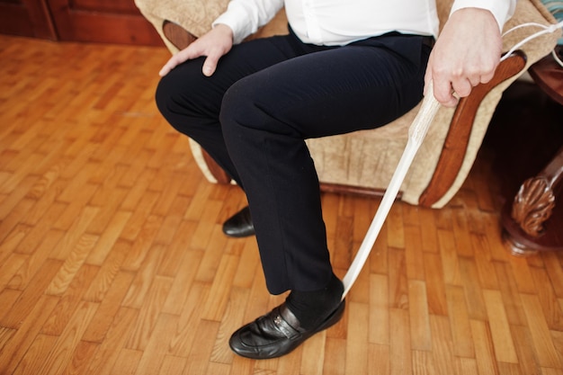 El hombre se pone zapatos negros clásicos con una cuchara de zapatos de madera