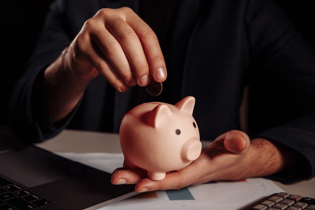 Hombre poniendo monedas en primer plano de la alcancía rosa. Concepto de ahorro.