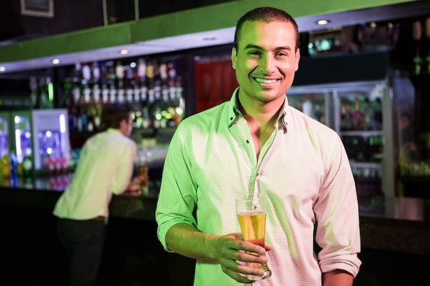 Hombre posando con un vaso de cerveza y un amigo en el bar