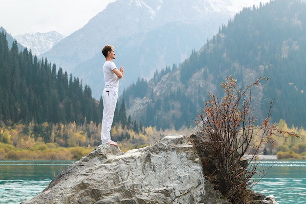 Un hombre en una pose de Samasthiti sobre una piedra entre un lago de montaña.