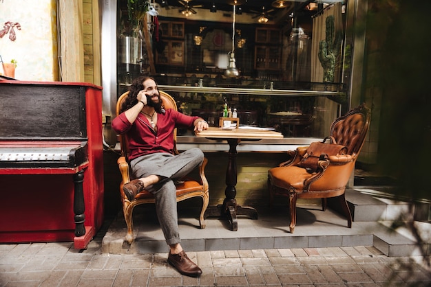 Hombre positivo alegre que tiene una conversación telefónica mientras está sentado en la mesa