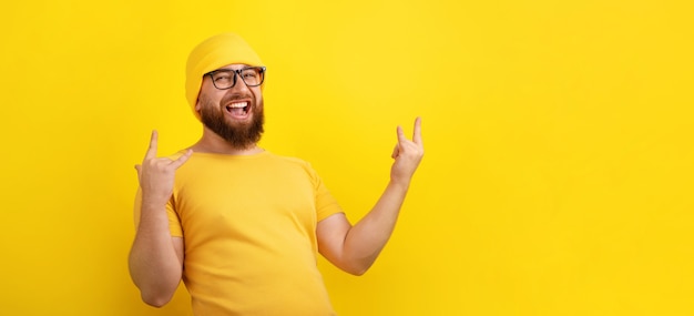 Hombre positivo hace gesto de rock n roll sobre fondo amarillo, concepto de lenguaje corporal y personas, diseño panorámico