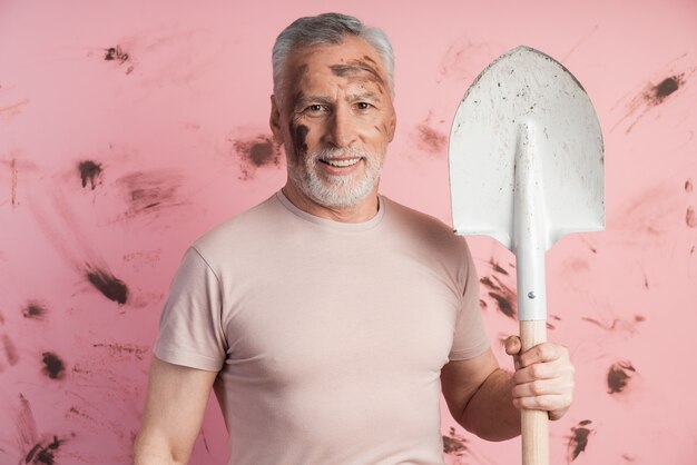 Hombre positivo con una pala en una pared de una pared rosada sucia