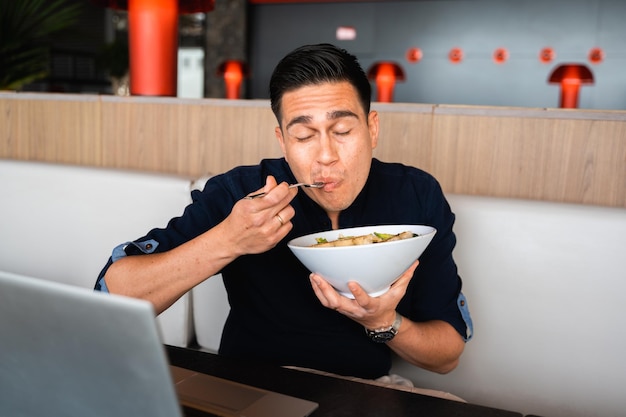 Hombre positivo sentado en la mesa comiendo una ensalada masticando