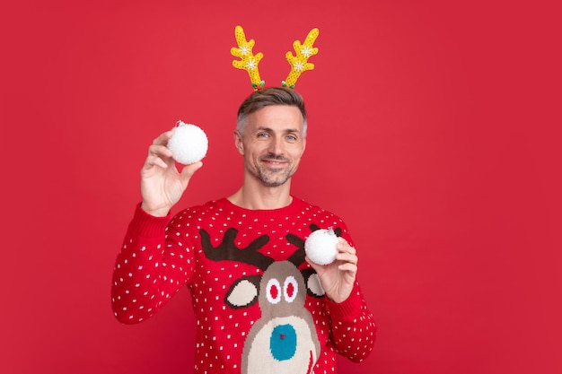 Hombre positivo en suéter de invierno y chico de astas de fiesta sostienen bolas de decoración de Navidad