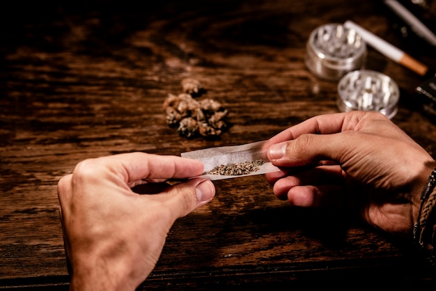 Un hombre practica con las manos cómo liar un porro de marihuana con papel de fumar.