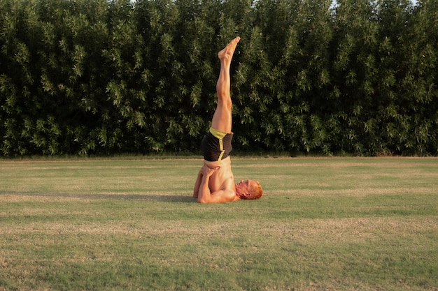 El hombre practica sarvangasana o pose de yoga para el hombro sobre el césped en el jardín iluminado por la luz del sol dorada