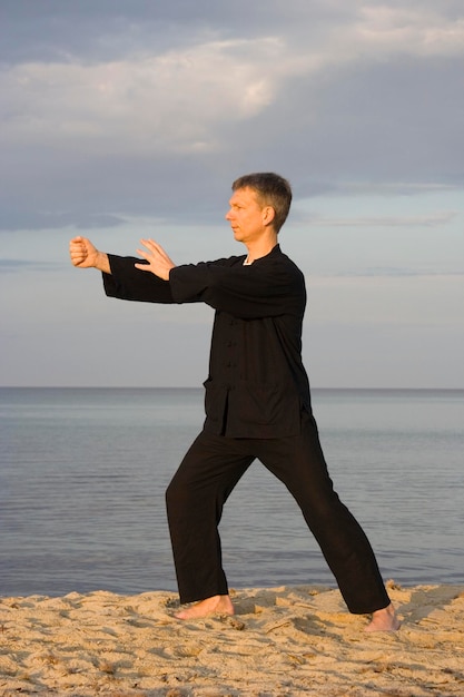 Foto hombre practicando artes marciales en una playa de arena contra el cielo