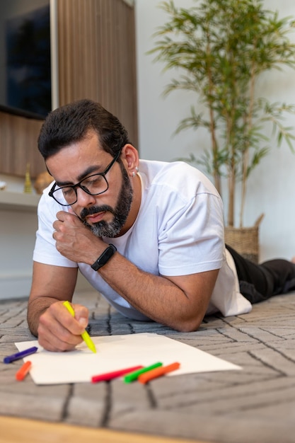 Hombre practicando terapia artística sentado en el salón de su casa pintando y dibujando con colore