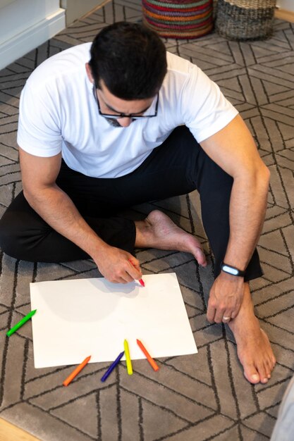 Hombre practicando terapia artística sentado en el salón de su casa pintando y dibujando con colore