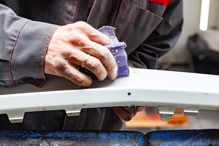 Un hombre prepara un elemento de la carrocería del automóvil para pintar después de un accidente con la ayuda de papel abrasivo en un taller de reparación de automóviles Parachoques de recuperación después de una colisión