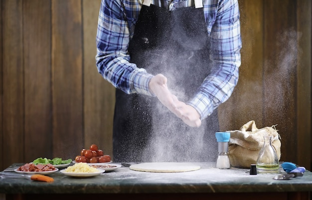 Un hombre prepara una pizza, amasa la masa y pone los ingredientes.