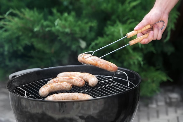 Hombre preparando deliciosas salchichas en parrilla al aire libre