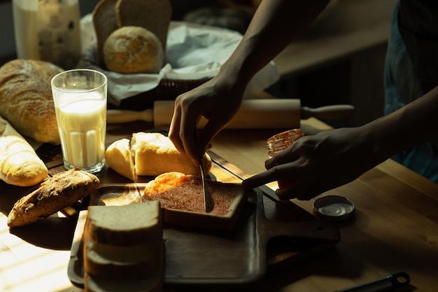 Hombre preparando un desayuno saludable esparciendo mermelada de fresa en una rebanada de pan sentado en la mesa de la cocina