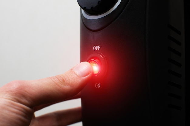 El hombre presiona el botón de encendido del radiador eléctrico de aceite de calefacción en el modo de sintonización de encendido o apagado del hogar Concepto de calefacción doméstica y conservación del calor Calentador lleno de aceite negro