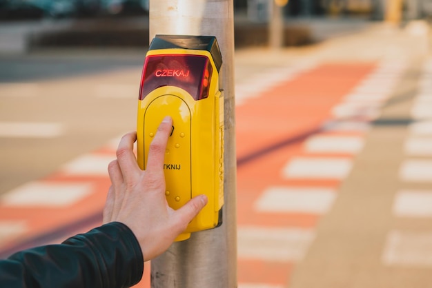 Hombre presionando el botón amarillo en un semáforo para peatones en el fondo de la carretera Botón de paso de peatones Czekaj dotknij Seguridad Polonia Seguridad polaca