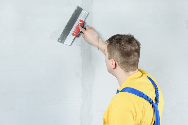 Un hombre procesa la pared con una espátula. Yesero en el trabajo.