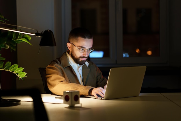 Hombre programador concentrado trabaja en la computadora portátil en la noche en la oficina vacía o corrección de errores en la aplicación