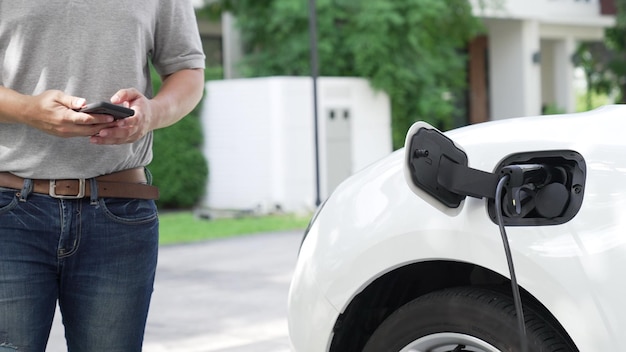 Un hombre progresista conecta un conector de alimentación libre de emisiones a la batería del vehículo eléctrico en su casa. Carga del vehículo eléctrico mediante un cable desde la estación de carga a la batería del vehículo eléctrico.