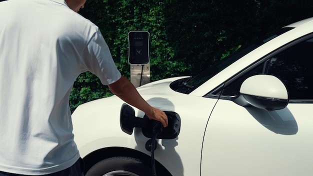 Hombre progresista instala el enchufe del cable de alimentación en su vehículo eléctrico Coche EV desde la estación de carga doméstica Coche eléctrico impulsado por energía limpia y renovable para preservar el medio ambiente Automóvil ecológico