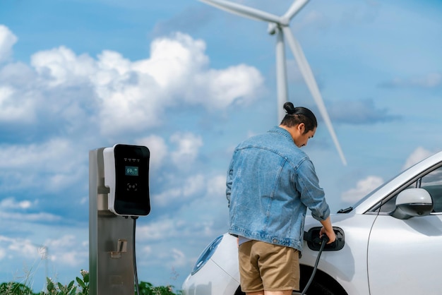 Hombre progresista con su automóvil EV y turbina eólica como concepto de energía renovable