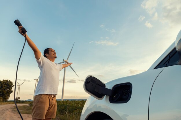 Hombre progresista con su automóvil EV y turbina eólica como concepto de energía renovable