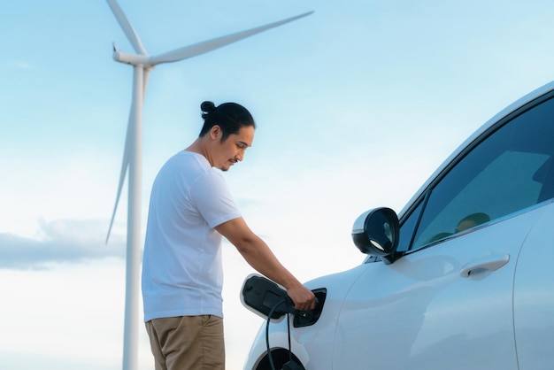 Hombre progresista con su automóvil EV y turbina eólica como concepto de energía renovable