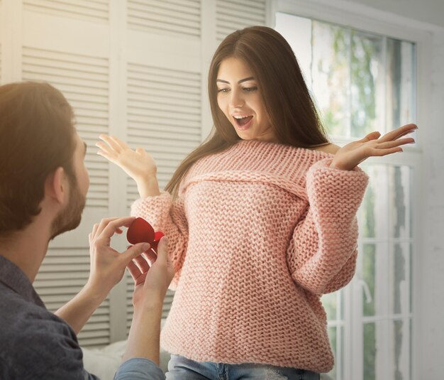 Foto hombre proponiendo a su mujer sorprendida en casa. niño feliz con anillo de compromiso haciendo una propuesta. concepto de amor, espacio de copia