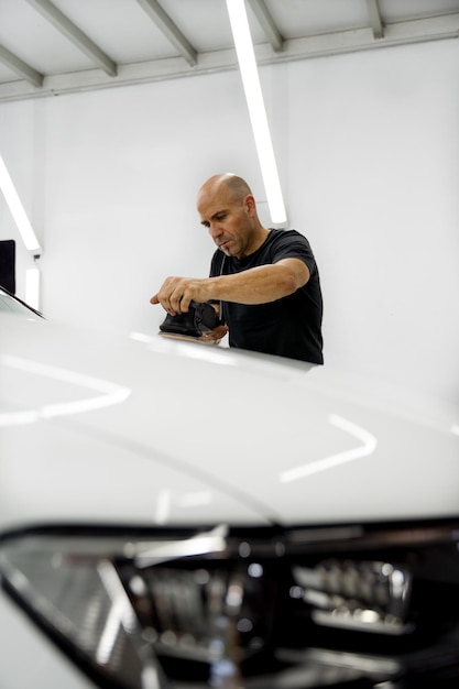 Hombre puliendo un coche blanco, vestido con una camiseta negra