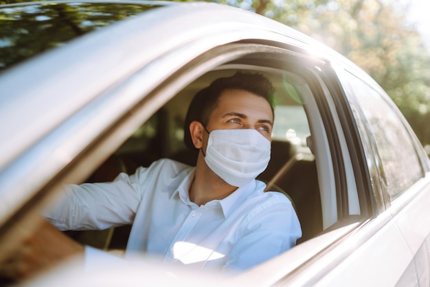 Foto un hombre que conducía un automóvil se pone una máscara médica durante una epidemia en una ciudad en cuarentena.