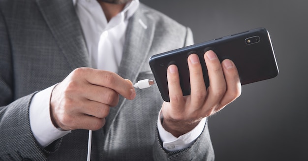 Hombre que conecta el cable del cargador al teléfono móvil.