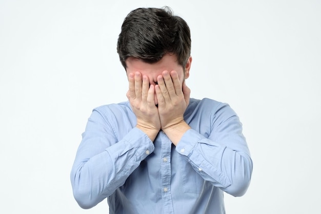 Hombre que cubre la cara con la mano mientras está de pie contra el fondo gris