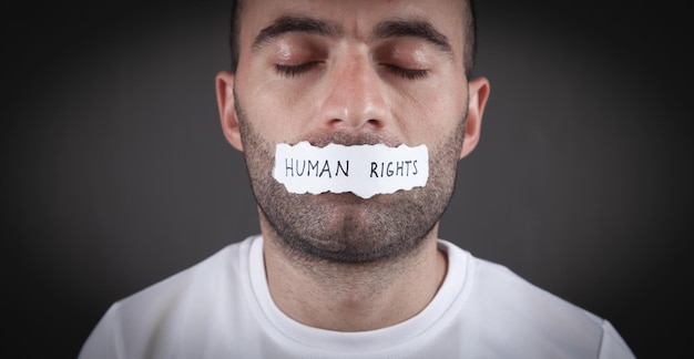 Hombre que cubre su boca con un texto de derechos humanos en papel rasgado