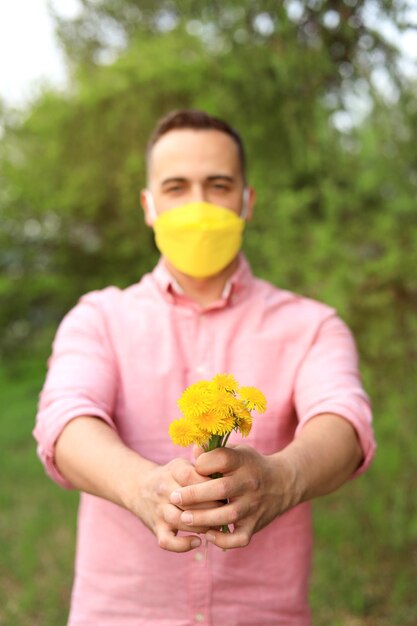 Un hombre que da un ramo de flores silvestres con una máscara médica en presencia de alergias