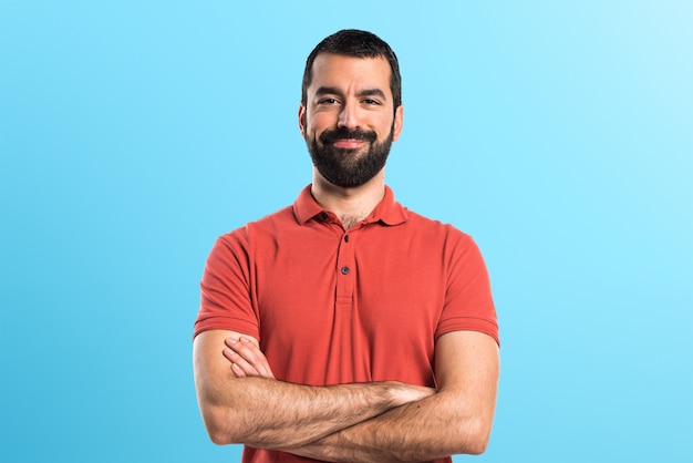 Hombre que desgasta la camisa roja del polo con sus brazos cruzados en fondo colorido