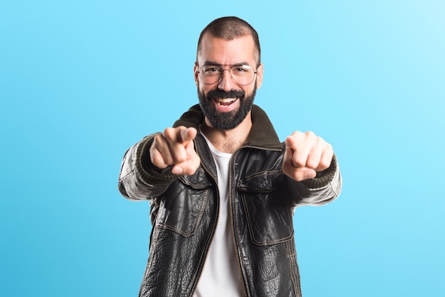 Hombre que desgasta una chaqueta de cuero que señala a la parte delantera en fondo colorido