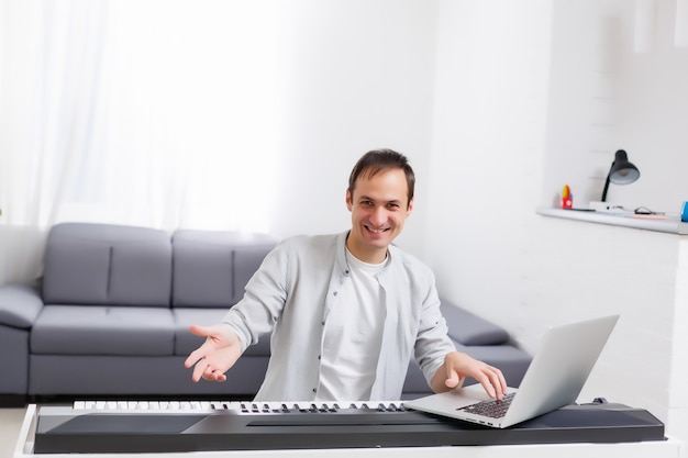 Un hombre que está aprendiendo a tocar el piano en línea con una computadora en casa. Conceptos de autodidacta, quedarse en casa y trabajar online