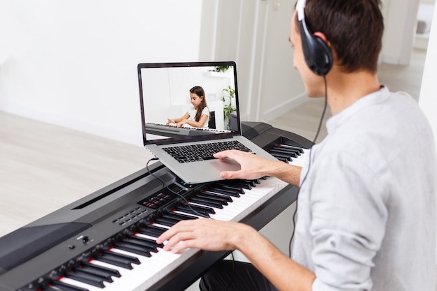 Un hombre que está aprendiendo a tocar el piano en línea con una computadora en casa. Conceptos de autodidacta, quedarse en casa y trabajar online