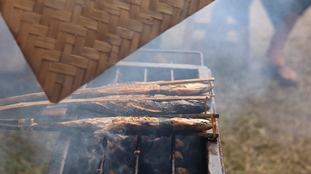 un hombre que está asando pescado tradicionalmente usa una parrilla para vender y ver el humo. Mariscos.