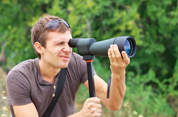 Hombre que está mirando con telescopio. Hombre positivo mirando a través de un telescopio