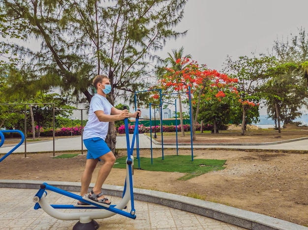 El hombre que hace ejercicios físicos empuja ejercicios de fuerza se inclina en el gimnasio de metal del parque público vacío al aire libre usando máscara solo para la prevención de Covid19 Estilo de vida saludable en cuarentena y coronavirus